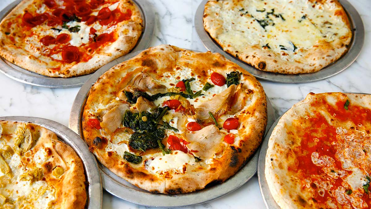 spread of different pizzas on metal plates on white marble table at Via Napoli Ristorante e Pizzeria (Italy) at Epcot in Orlando, Florida, USA